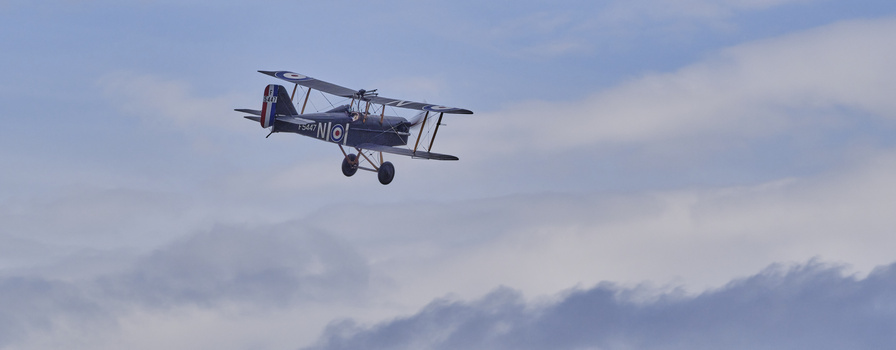 Vintage biplane in flight against a cloudy blue sky.