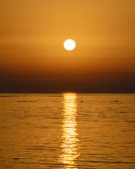 Bright sun reflecting across calm ocean waters at golden hour during sunset.
