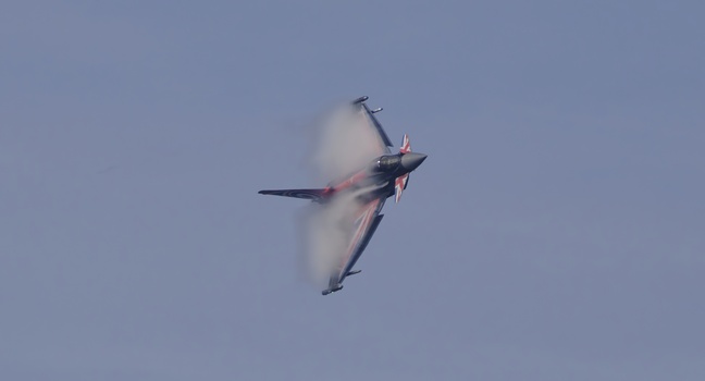Fighter jet performing high-speed maneuver with vapor cloud formation around fuselage.