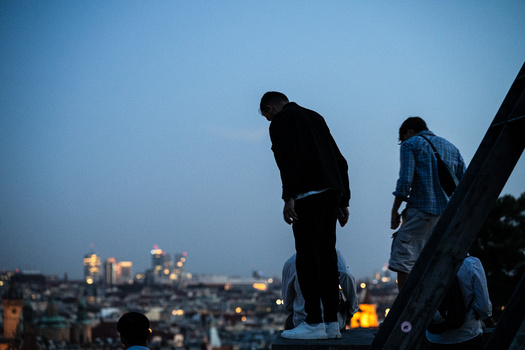 Silhouetted figures standing on a ledge with a cityscape glowing at dusk in the background.