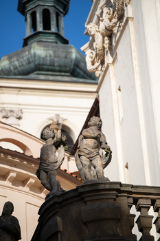 Stone sculptural relief of two figures on an ornate architectural pediment with a copper dome above.