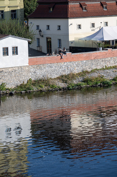 Waterfront buildings with red-brick and white walls reflected in calm water with blue sky.