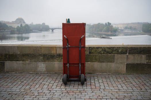 Red metal cart positioned against a concrete barrier overlooking a river and cityscape.
