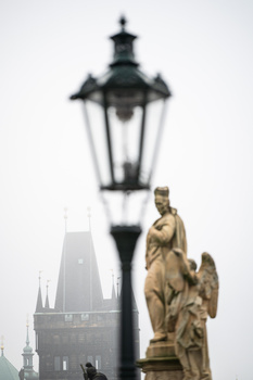 Golden angel statue with architectural lamp and Gothic spires in soft, overcast light.