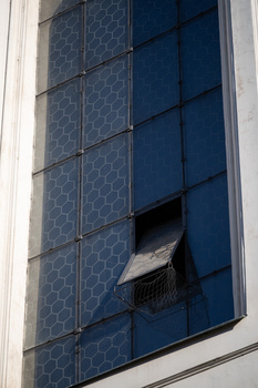 Modern building facade with blue hexagonal patterned solar panels and a broken window pane.