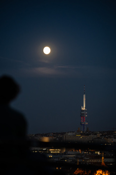 Full moon rising above a distant illuminated communications tower in twilight.