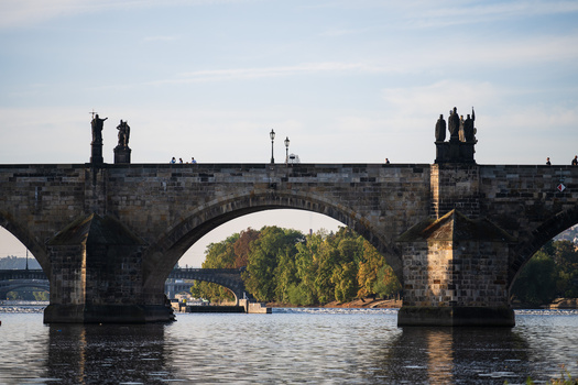 Historic stone bridge with multiple arches spanning a river, featuring ornamental towers at each end.