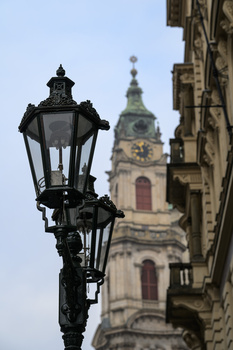 Black ornate street lamp in sharp focus with baroque church tower blurred in background.