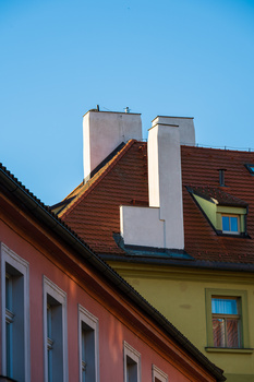 Colorful European building facades with contrasting chimneys and tile roofing against clear blue sky.
