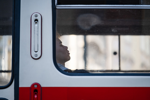 Silhouette of a person's profile visible through a bus window with white and red exterior paneling.