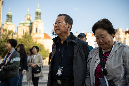 Two people wearing lanyards stand in foreground with golden-domed churches visible behind them.