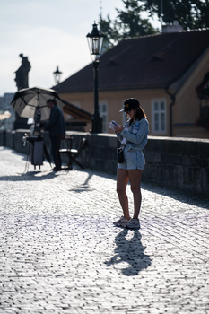Woman standing on cobblestone street in dappled sunlight, wearing a denim jacket and sneakers.