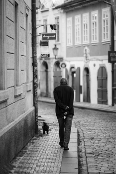 Man walking alone down a narrow European cobblestone street lined with historic buildings.