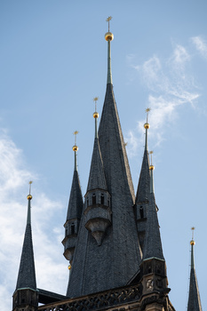 Gothic castle tower with multiple spires against blue sky with white clouds.