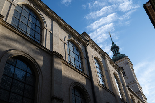 Neoclassical building facade with large arched windows and a copper spire against blue sky.