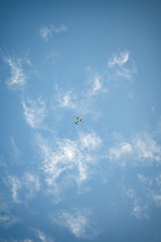 Small aircraft flying through scattered white clouds against a clear blue sky.
