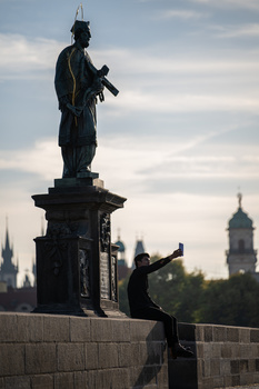 Silhouetted statue of a figure holding a rifle atop a stone pedestal against a cloudy sky.