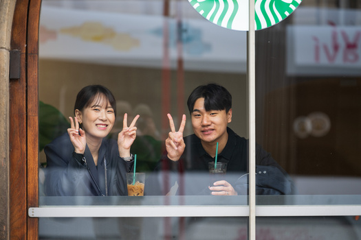 Two young people making peace signs while looking out through a Starbucks window.