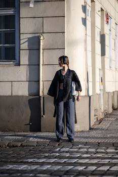 Woman in dark clothing standing on cobblestone street beside historic building with stone facade.