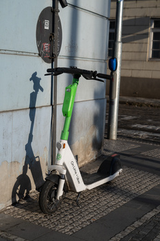 Green and white electric scooter parked against a metal cylindrical tank on a brick paved surface.