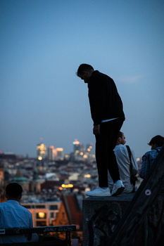 Silhouetted figure standing on structure against twilight cityscape.