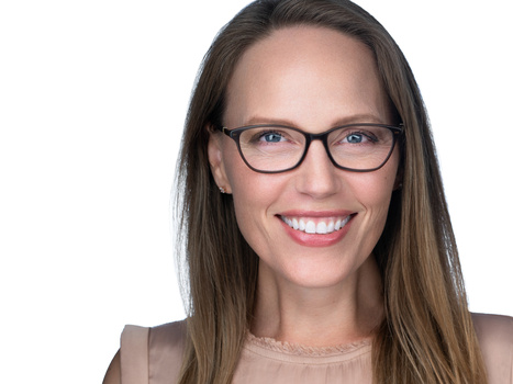 Woman wearing glasses smiling at camera against white background.