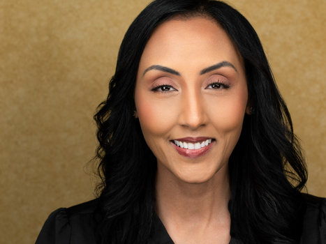 Professional headshot of a woman with long dark hair against a neutral tan background.