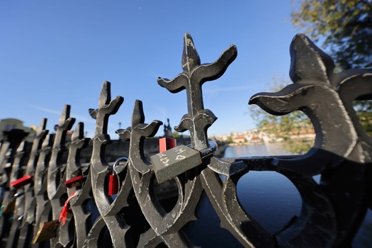 Ornate wrought iron fence with cross-topped pickets in sharp focus, with blurred crosses and red flowers receding into background.