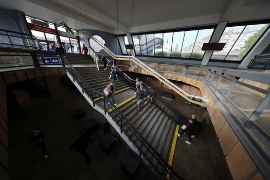 Modern transit station interior with multiple staircases and natural light from skylights above.