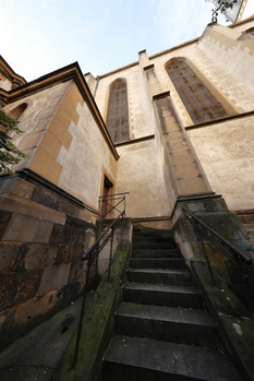 Stone building facade with steep staircase ascending between weathered walls, shot from ground level upward.