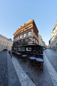 Historic corner building with ornate golden facade and ground-floor storefront on European cobblestone street.