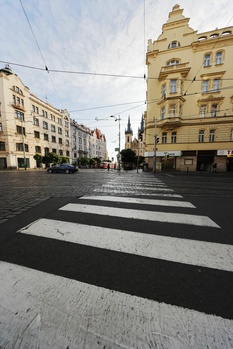 Zebra crosswalk stretches into an urban square flanked by classical architecture and overhead power lines.