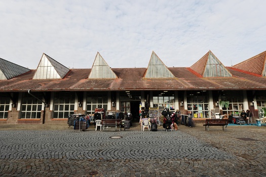 Historic brick building with distinctive peaked roof dormers and large storefront windows on a herringbone-patterned plaza.