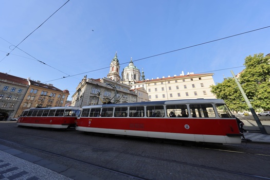 Red and white tram on tracks with ornate church and historic buildings in background under clear blue sky.