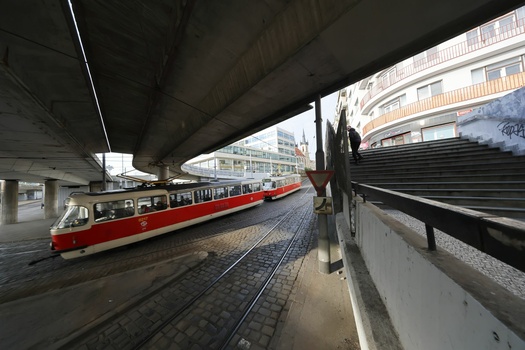 Red and white tram stopped beneath an elevated concrete highway structure in an urban setting.