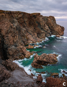 Rugged coastal cliffs with turquoise waters and white waves crashing against rocky outcrops.