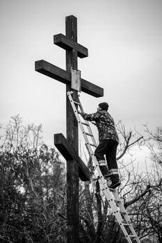 Person on ladder securing a large wooden cross against a winter sky.