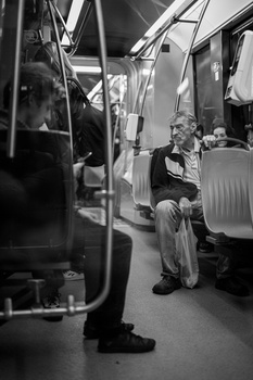 Black and white photograph of an elderly person sitting alone inside a public transit vehicle.