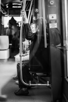 Black and white photograph of a person inside a public transit vehicle, holding a vertical pole with their hand raised.