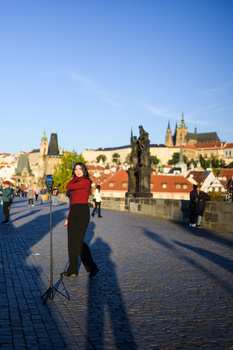Runner in red shirt on Charles Bridge in Prague, with castle and cathedral in golden afternoon light.