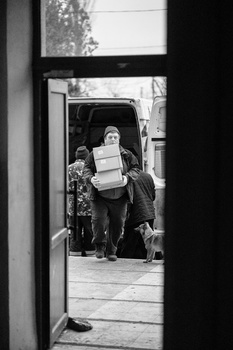 People exiting a vehicle through an open door, framed by a dark doorway in the foreground.