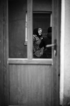 Woman looking out through a partially open doorway in a black and white portrait.