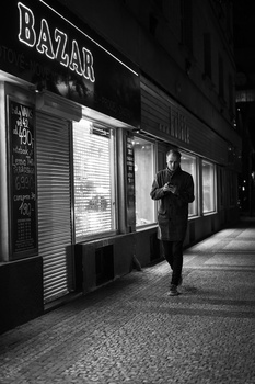 Man jogging past closed storefront with BAZAR sign at night