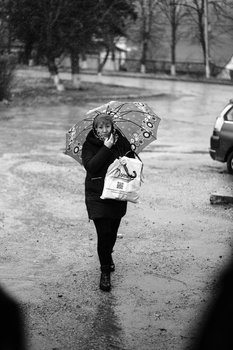 Woman walking in rain holding a patterned umbrella on a wet street.