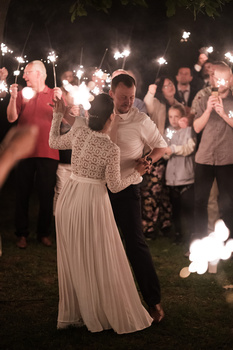 Couple dancing at nighttime outdoor wedding reception surrounded by guests holding illuminated sparklers.