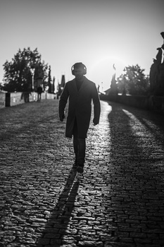 Man jogging away from camera on wet cobblestone street at dusk with trees lining the path.