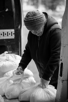 Person in winter hat and dark jacket handling large white plastic bags outdoors.