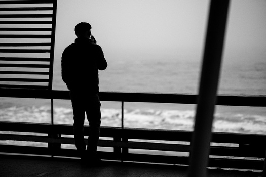 Silhouetted figure standing at a railing overlooking a rough ocean, photographed through geometric linear elements.