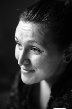 Black and white portrait of a woman with pulled-back hair, looking toward camera with a subtle smile against dark background.