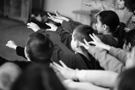 Multiple people with hands raised together in a circle, captured in black and white.